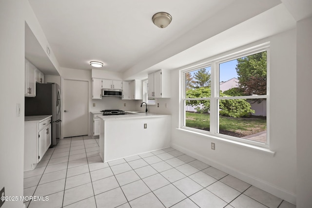 kitchen featuring stainless steel microwave, a sink, a peninsula, white cabinets, and light countertops