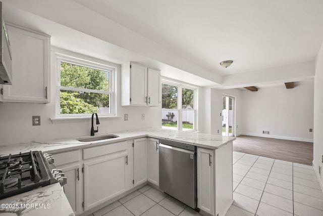 kitchen featuring stainless steel dishwasher, a sink, light tile patterned floors, a peninsula, and white cabinetry