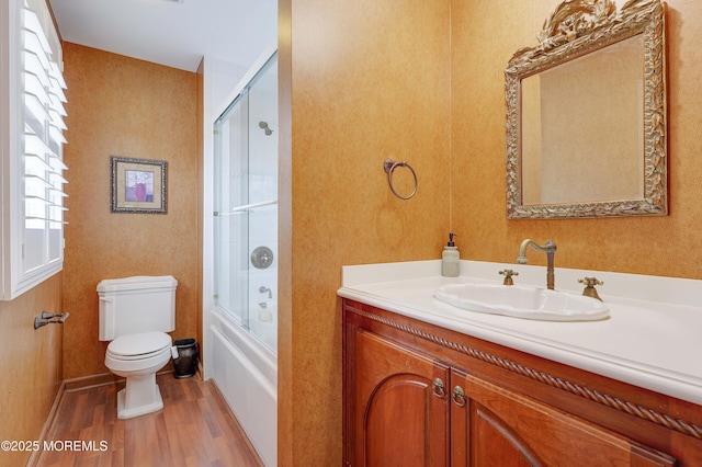 bathroom with wood finished floors, toilet, vanity, and bath / shower combo with glass door