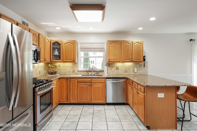 kitchen featuring appliances with stainless steel finishes, a sink, a peninsula, a breakfast bar area, and light stone counters