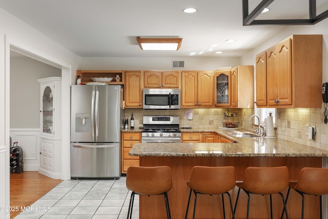 kitchen with appliances with stainless steel finishes, a sink, a peninsula, glass insert cabinets, and a kitchen breakfast bar