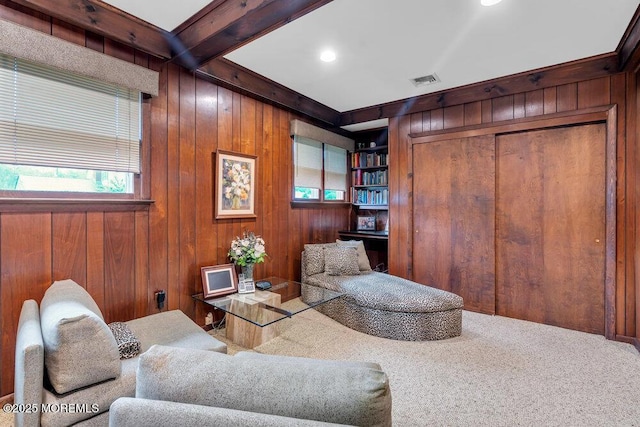 carpeted living area with wood walls, plenty of natural light, and beam ceiling