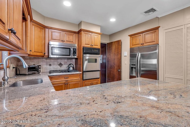 kitchen with appliances with stainless steel finishes, a sink, a warming drawer, light stone counters, and backsplash