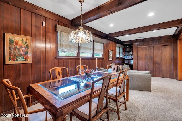 carpeted dining space featuring wood walls, a chandelier, and beam ceiling