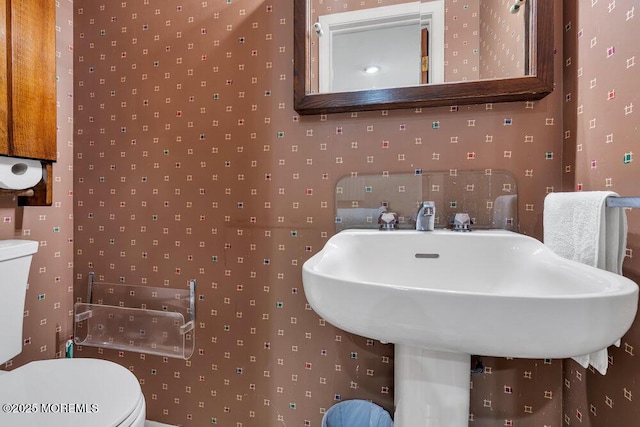 half bath with wallpapered walls and toilet