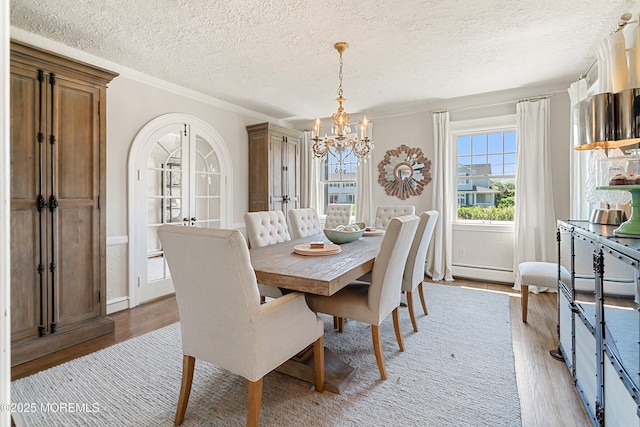 dining space featuring a chandelier, plenty of natural light, a baseboard heating unit, light wood finished floors, and crown molding