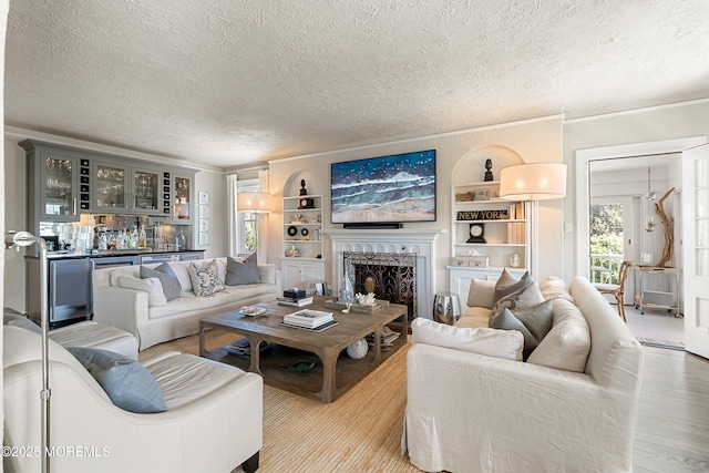 living room featuring a textured ceiling, wood finished floors, a fireplace, built in features, and ornamental molding
