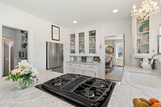 kitchen featuring freestanding refrigerator, stovetop with downdraft, a sink, white cabinets, and glass insert cabinets