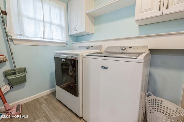 laundry room featuring washing machine and dryer, cabinet space, light wood-style floors, and baseboards