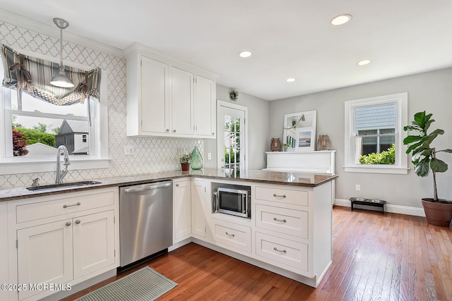 kitchen with appliances with stainless steel finishes, a sink, a peninsula, white cabinetry, and wood-type flooring