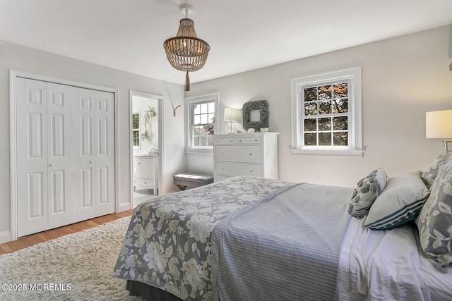 bedroom with wood finished floors, a chandelier, ensuite bathroom, a closet, and baseboards