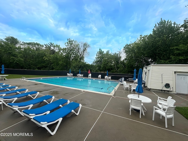 community pool with fence, a patio area, and view of wooded area