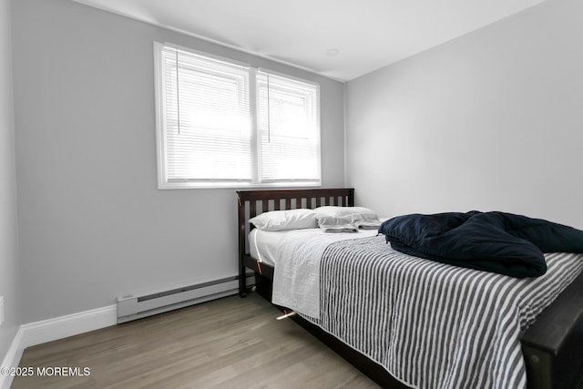 bedroom featuring a baseboard heating unit, wood finished floors, and baseboards