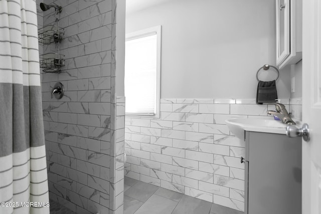 bathroom with tiled shower, vanity, tile walls, and a wainscoted wall