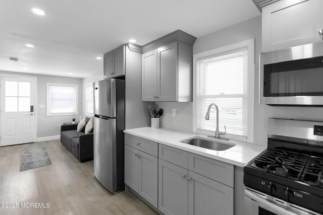 kitchen with stainless steel appliances, a sink, gray cabinets, light countertops, and light wood finished floors