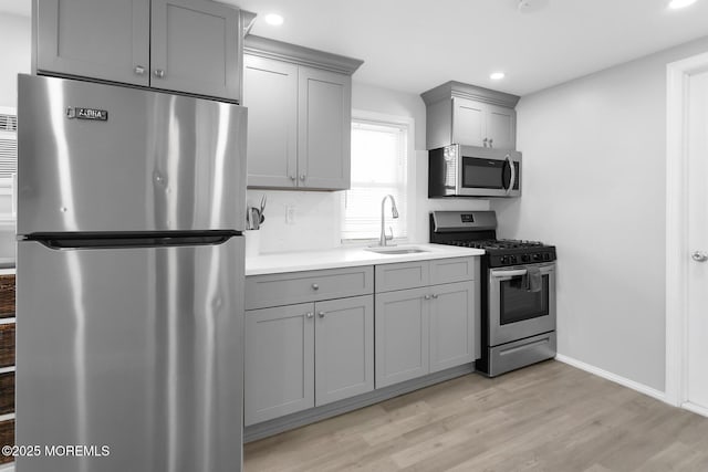 kitchen featuring stainless steel appliances, gray cabinetry, a sink, light wood-style flooring, and recessed lighting