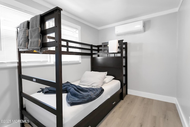 bedroom featuring an AC wall unit, wood finished floors, baseboards, and ornamental molding