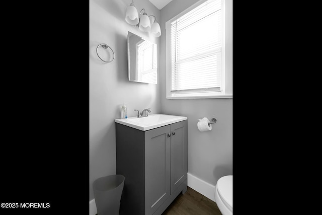 half bathroom featuring toilet, wood finished floors, vanity, and baseboards