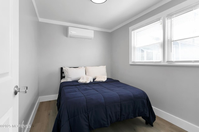 bedroom with an AC wall unit, crown molding, baseboards, and wood finished floors