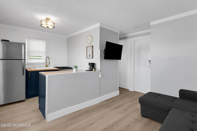 kitchen with freestanding refrigerator, blue cabinets, light wood-style floors, crown molding, and a textured ceiling