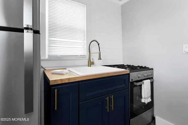 kitchen with stainless steel appliances, blue cabinetry, butcher block counters, and a sink
