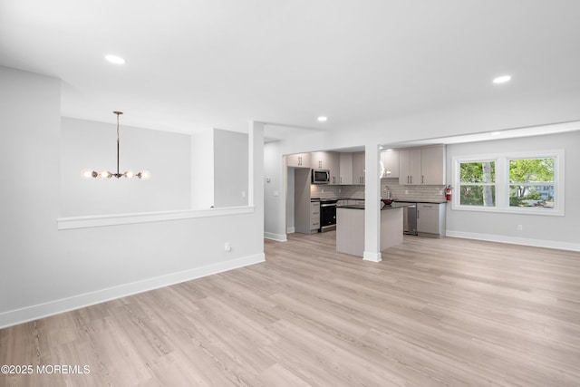unfurnished living room with light wood finished floors, a chandelier, baseboards, and recessed lighting