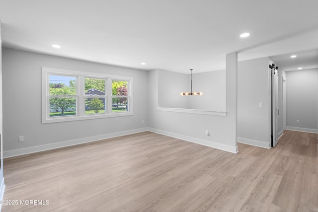 spare room with light wood finished floors, a chandelier, recessed lighting, a barn door, and baseboards