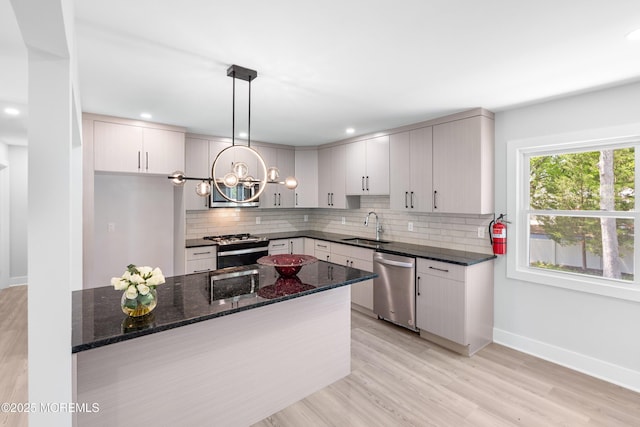 kitchen with appliances with stainless steel finishes, a sink, tasteful backsplash, baseboards, and dark stone countertops