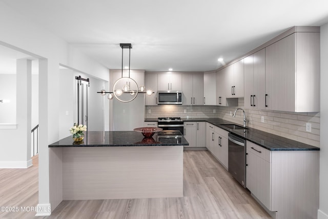 kitchen with appliances with stainless steel finishes, a sink, decorative backsplash, light wood-type flooring, and a barn door