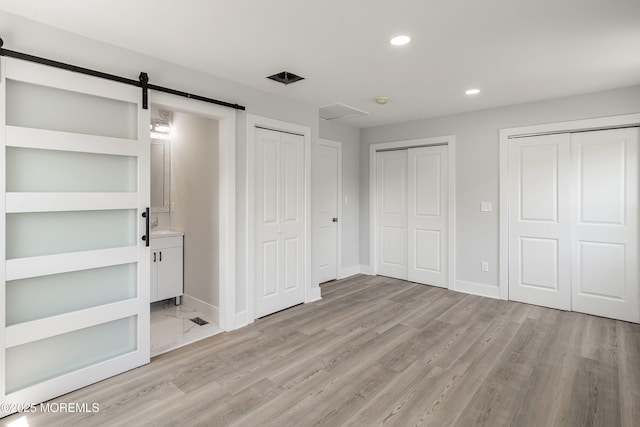 unfurnished bedroom with a barn door, two closets, recessed lighting, light wood-style flooring, and baseboards