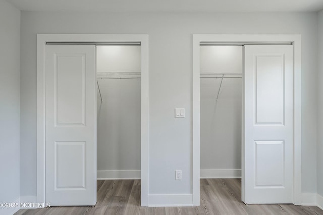 unfurnished bedroom with wood finished floors, multiple closets, and baseboards