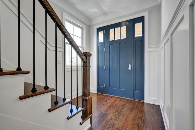 foyer entrance featuring a decorative wall, stairs, dark wood finished floors, and wainscoting