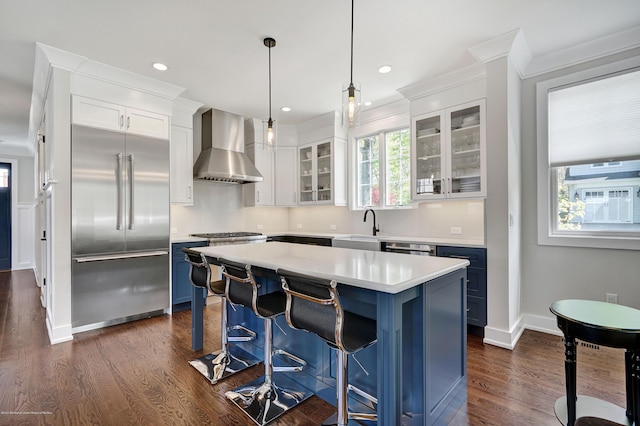 kitchen featuring built in fridge, wall chimney range hood, blue cabinets, white cabinets, and crown molding