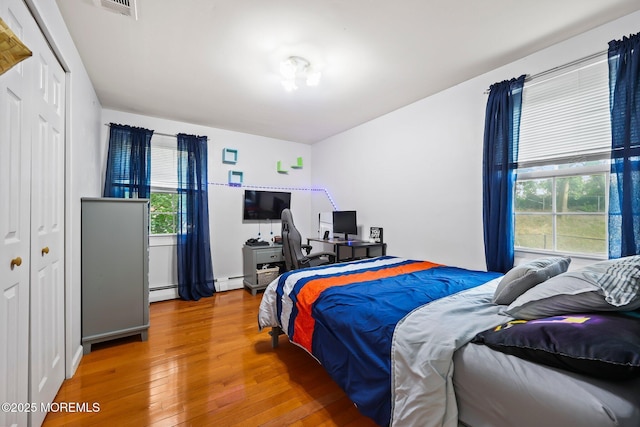 bedroom featuring wood finished floors, a desk, a closet, and a baseboard heating unit
