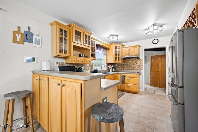 kitchen with freestanding refrigerator, a peninsula, a sink, tasteful backsplash, and a breakfast bar