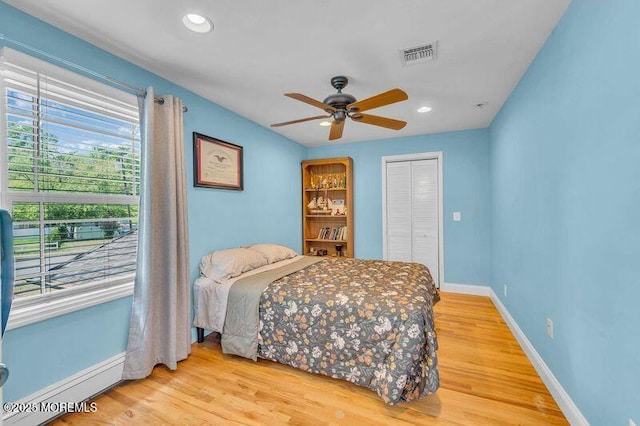 bedroom featuring a baseboard radiator, baseboards, light wood finished floors, a closet, and a ceiling fan