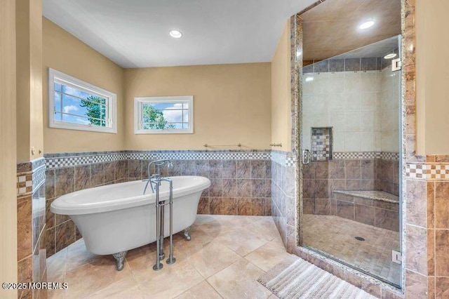 bathroom featuring tile walls, a stall shower, a wainscoted wall, a soaking tub, and tile patterned floors