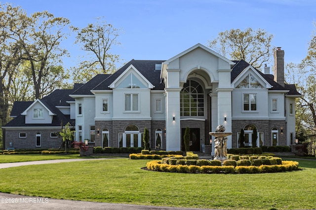 view of front of property featuring stucco siding, stone siding, a front yard, and a chimney