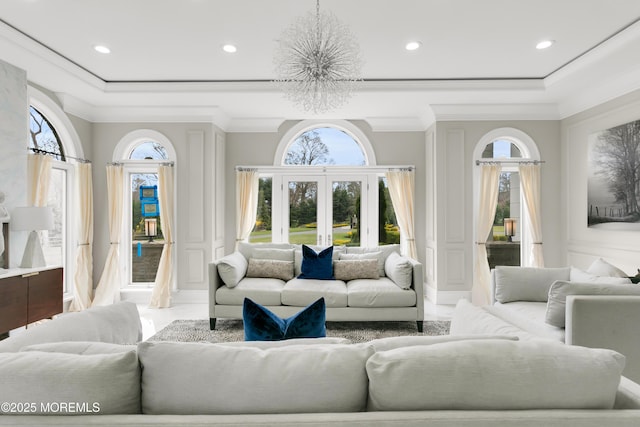 living area featuring a decorative wall, a raised ceiling, healthy amount of natural light, a chandelier, and crown molding