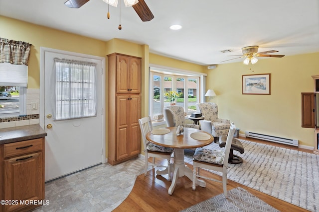 dining area featuring a baseboard heating unit, a ceiling fan, light wood-style flooring, and baseboards