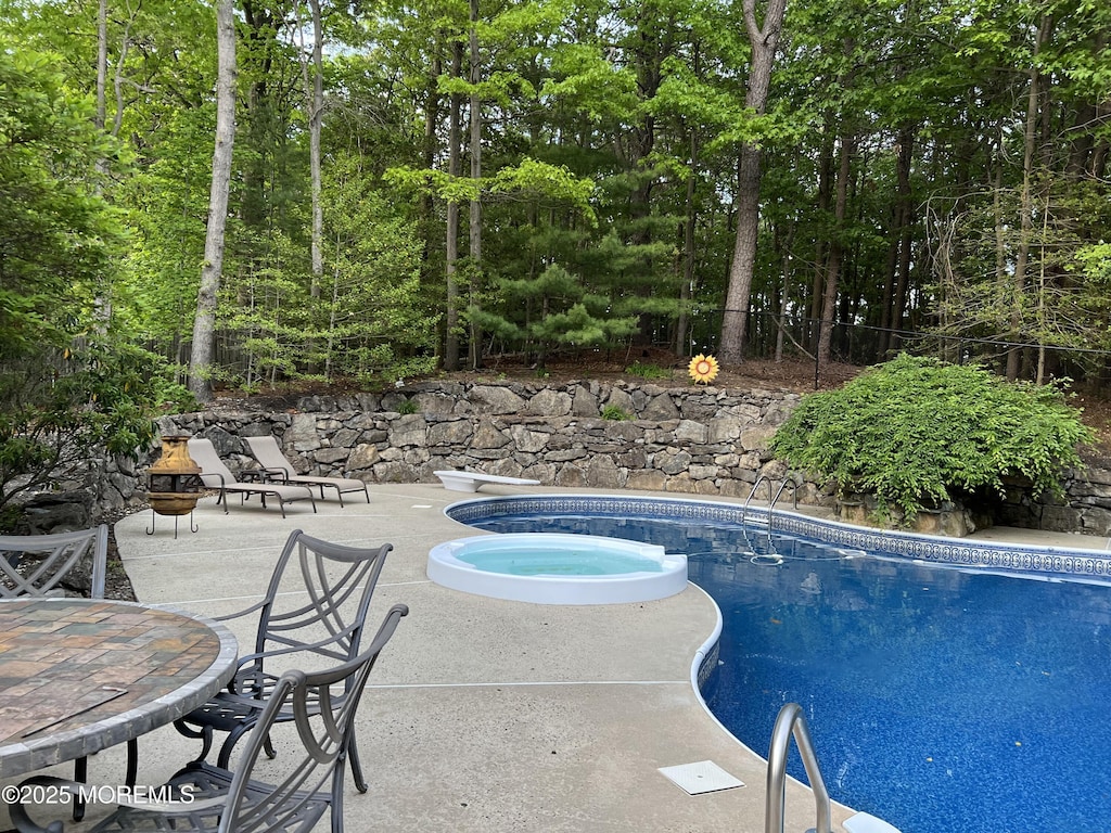 outdoor pool with a patio area, a diving board, and an in-ground hot tub