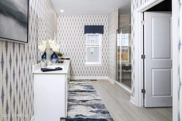 full bathroom with wallpapered walls, baseboards, a stall shower, wood tiled floors, and vanity