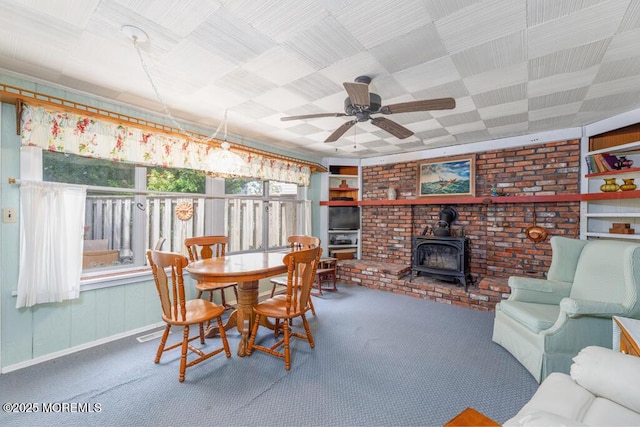 carpeted dining space featuring a wood stove, a ceiling fan, and baseboards
