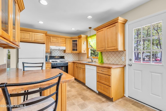 kitchen with white appliances, under cabinet range hood, a sink, decorative backsplash, and decorative light fixtures
