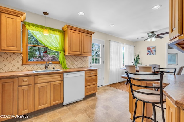 kitchen featuring white dishwasher, a sink, backsplash, ceiling fan, and hanging light fixtures