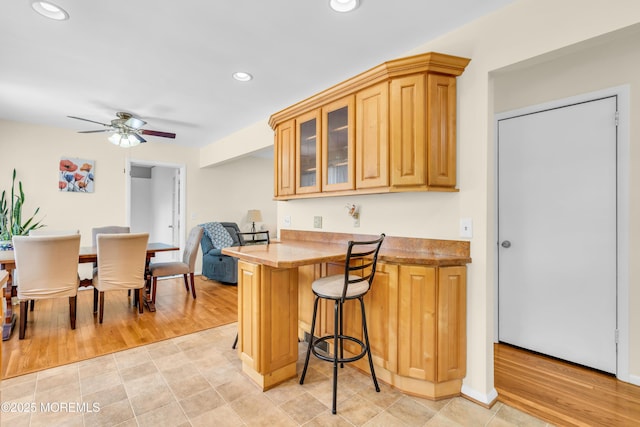 kitchen featuring a breakfast bar, recessed lighting, glass insert cabinets, a ceiling fan, and a peninsula