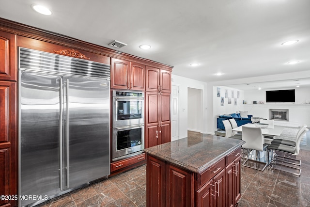 16 Bridle Dr, West Long Branch, NJ 07764 - kitchen featuring appliances with stainless steel finishes, a kitchen island, dark stone countertops, reddish brown cabinets, and recessed lighting