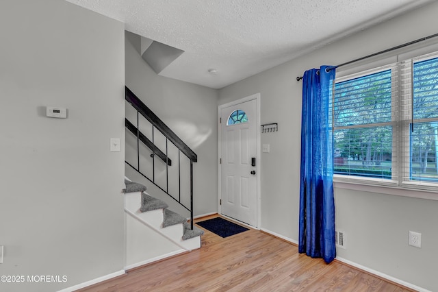 foyer entrance with wood finished floors, healthy amount of natural light, baseboards, a textured ceiling, and stairway