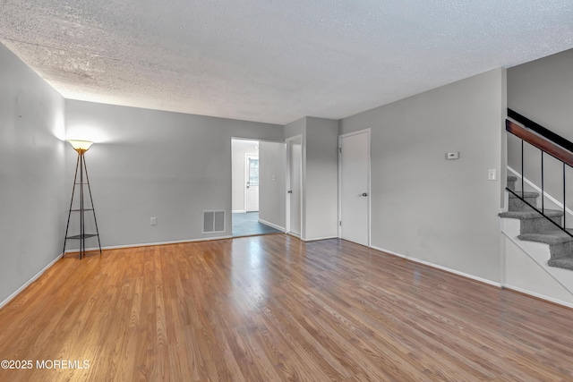 unfurnished living room with wood finished floors, a textured ceiling, stairs, and baseboards