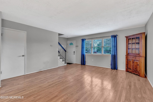unfurnished living room with light wood finished floors, stairway, a textured ceiling, and baseboards